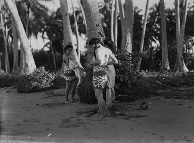 [Candid portrait of three young Polynesian women standing at the base of a palm tree]