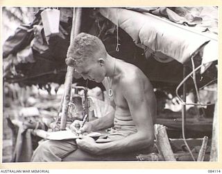 SWAN BEACH, JACQUINOT BAY. NEW BRITAIN. 1944-12-10. PRIVATE M. BEET, D COMPANY, 16 INFANTRY BATTALION, 13 INFANTRY BRIGADE, WRITING HOME OUTSIDE HIS HUMPY CONSTRUCTED FROM BANANA LEAVES AND COCONUT ..