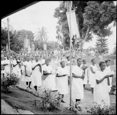 Women holding books in the Corpus Christi Procession with volcanic eruption smoke in the background, Vunapope Sacred Heart Mission, Kokopo, New Guinea, 1937 / Sarah Chinnery