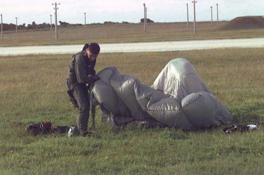 Right side front view medium shot of US Marine Lance Corporal Arguemedo, parachute rigger, 5th Force Reconnaissance Battalion, 3rd Marine Division, as he gathers up his MC5 parachute after successfully jumping from a US Air Force C-141 Starlifter during the Force Reconnaissance Exercise