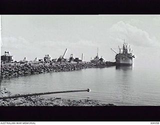 LORENGAU, ADMIRALTY ISLANDS. 1947-07. NABU WHARF, LOOKING SEAWARDS. THE WHARF IS LITTERED WITH A VARIETY OF CONSTRUCTION EQUIPMENT. ALONGSIDE IS THE ATTACK TRANSPORT USS LEO (AKA-60) LOADING ..