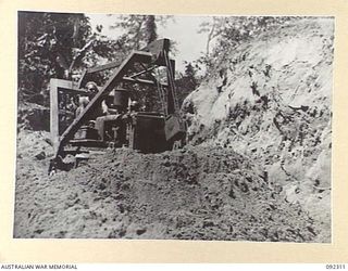 BOUGAINVILLE, 1945-05-18. SAPPER H. POWELL, 15 FIELD COMPANY, ROYAL AUSTRALIAN ENGINEERS, MANS A BULLDOZER TO BREAK DOWN THE ESCARPMENT SOUTH OF HONGORAI RIVER ON COMMANDO ROAD. THIS WILL ALLOW ..