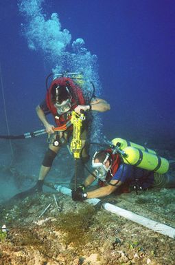 MASTER CHIEF (UCCM) Michael R. Oliver and Construction Mechanic Second Class (CM2) (SCW/DV) David Power, both from Underwater Construction Team Two (UCT-2), drill holes in the coral bed next to the cable so that clamps can be placed for stabilization at the Pacific Missile Range Facility off Kauai, Hawaii