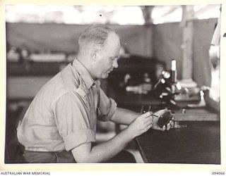 TOROKINA, BOUGAINVILLE, 1945-07-16. CAPT A.K. SEWELL IN THE PATHOLOGY DEPARTMENT AT 106 CASUALTY CLEARING STATION EXAMINING A CULTURE PLATE