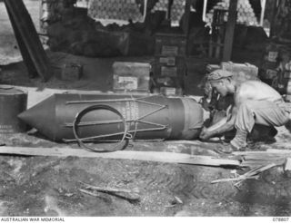 TOROKINA, BOUGAINVILLE ISLAND. 1945-01-29. WARRANT OFFICER I.A. BRUN, SOLOMON'S DETACHMENT, 12TH AIR MAINTENANCE PLATOON (TS), 4TH BASE SUB AREA, TUCKING THE STATIC LINE INTO THE PARACHUTE PACK ON ..