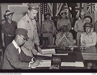 TOROKINA, BOUGAINVILLE. 1945-09-08. LIEUTENANT-GENERAL (LT-GEN) M. KANDA, COMMANDER, 17TH JAPANESE ARMY, SIGNING THE INSTRUMENT OF SURRENDER DURING A FORMAL SURRENDER CEREMONY AT HQ 2 CORPS. THE ..
