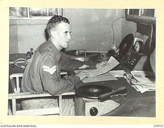 BOSLEY FIELD, BOUGAINVILLE, SOLOMON ISLANDS. 1945-03-15. NX163160 CORPORAL T. ROBERTS OF EARLWOOD, NSW, ANNOUNCER, AUSTRALIAN ARMY BROADCASTING STATION, AT THE MICROPHONE AND TURN-TABLES IN THE ..