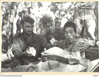 PAPUA, NEW GUINEA. 1942-10. JAPANESE PRISONER CAPTURED NEAR NAURO. HE HAD BEEN OVERWORKED AND WAS NEARLY STARVING WHEN TAKEN PRISONER. HE IS SEEN BEING CARED FOR BY AUSTRALIAN STRETCHER BEARERS