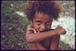 Child with shy expression, hiding part of face behind arm