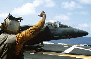 A plane director on the flight deck of the amphibious assault ship USS SAIPAN (LHA-2) signals to the pilot of an AV-88 Harrier aircraft attached to Marine Medium Helicopter Squadron 261 (HMM-261) during a rehearsal for Operation Sharp Edge. The SAIPAN is on station off the coast of Liberia