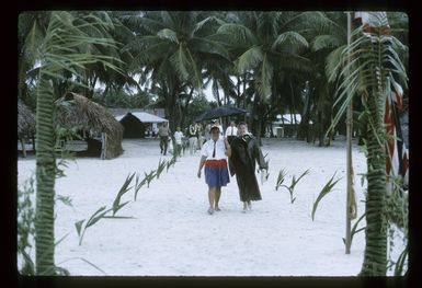 Two unidentified women walking on a path marked by palm fronds, during Sir Arthur Porritt's state visit to Palmerston Island
