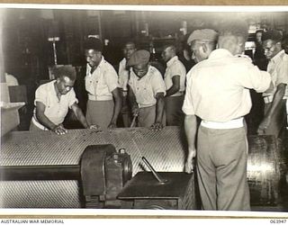 NEWCASTLE, NSW. 1944-01-28. AUSTRALIAN AND NEW GUINEA ADMINISTRATION UNIT NATIVES INSPECTING A CHECKER ROLL AT THE BROKEN HILL PTY., STEEL ROLLING MILLS