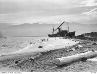 Malahang, New Guinea. 1943-09. A Piper Cub aircraft on patrol at the surfing beach of Malahang swoops over relaxing troops and the wreck of the Japanese ship Myokomaru