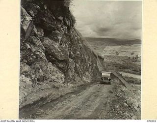 WAU - LAE ROAD, 1944-02-26. A ROAD SHELF CUT 16 FEET WIDE INTO THE SIDE OF A 60 DEGREE SLOPE 200 FEET ABOVE RIVER LEVEL. THIS ROAD SECTION THIRTY-ONE AND A HALF MILES FROM WAU, MAINTAINED BY THE ..