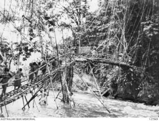 NEAR BOBDUBI, NEW GUINEA. 1943-07. NATIVE CARRIERS CROSSING THE KUNDA BRIDGE OVER THE FRANCISCO RIVER ON THE WAY FORWARD TO THE 58TH/59TH BATTALION. THE TWO NATIVE BEARERS IN THE CENTRE OF THE ..