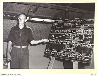 JACQUINOT BAY, NEW BRITAIN, 1945-08-25. LIEUTENANT M.H. THEW, LECTURER, NO. 2 MOBILE TEAM LAND HEADQUARTERS SCHOOL OF ARMY EDUCATION, EXPLAINING THE ORGANISATION OF THE MINISTRY OF POST WAR ..