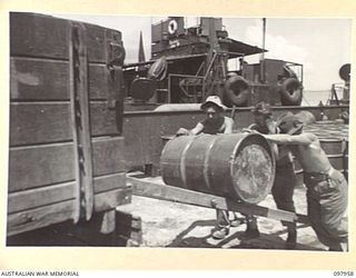 WEWAK BEACH, NEW GUINEA. 1945-10-18. MEMBERS OF 8 PORT OPERATING COMPANY ROLLING FUEL DRUM UP A WOODEN RAMP ONTO A TRUCK. THE STORES ARE BEING TRANSPORTED FROM THE LANDING CRAFT, TANK ON WEWAK ..