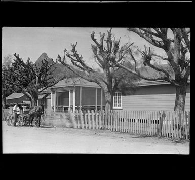 The Cook Islands Trading Company house with picket fence and unidentified people on a horse drawn wagon in front, Rarotonga, Cook Islands