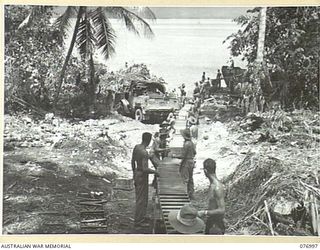 JACQUINOT BAY, NEW BRITAIN. 1944-11-18. TROOPS OF THE 55TH SUPPLY DEPOT PLANTOON UNLOADING SUPPLIES FROM A BARGE BY MEANS OF ROLLERS AT THE PALMALMAL PLANTATION