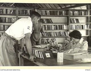 PORT MORESBY, PAPUA, 1944-02-25. MISS S. GRAHAM (1), AN AUSTRALIAN RED CROSS SOCIETY WORKER, WHO IS IN CHARGE OF THE RED CROSS SECTION AT THE 2/1ST GENERAL HOSPITAL, CHANGES A PATIENT'S BOOK AT THE ..