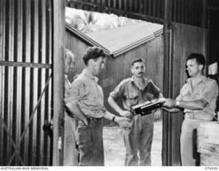 LAE, NEW GUINEA. 1944-10-04. SX32659 LIEUTENANT C.H. MORRIS ISSUING RUM FORM THE SPIRIT STORE OF THE AUSTRALIAN ARMY CANTEENS SERVICE BULK STORE, NEW GUINEA DETACHMENT