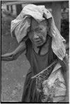 Mortuary ceremony: elderly woman, Bomtavau, wearing head cloth carries banana leaf bundle (wealth item) in basket