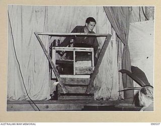 JACQUINOT BAY, NEW BRITAIN. 1945-04-15. PTE F.E. QUIGLEY, 5 BASE SUB-AREA LANDING SHIP DETACHMENT, PLAYING HIS SET OF HOME MADE DRUMS, WHICH CONSISTS OF THREE TINS, A WOODEN BOX, BEER BOTTLE AND ..