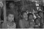 People smoke and chew betel nut, in shade under the awning of a shelter