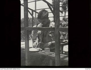 MOMOTE, LOS NEGROS ISLAND, ADMIRALTY ISLANDS. 1944-03-08. RAAF KITTYHAWK PILOT EATING HIS LUNCH STANDING AT A BENCH ALONG THE FRAMEWORK OF A WALL IN A PARTLY ERECTED CREW-ROOM NEAR THE AIRSTRIP. ..