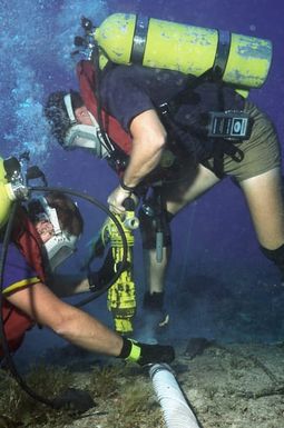 MASTER CHIEF (UCCM) Michael R. Oliver and Construction Mechanic Second Class (CM2) (SCW/DV) David Power, both from Underwater Construction Team Two (UCT-2), drill holes in the coral bed next to the cable so that clamps can be placed for stabilization at the Pacific Missile Range Facility off Kauai, Hawaii