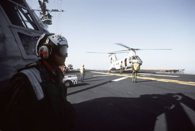 Flight deck crewmen stand by as a Marine Medium Helicopter Squadron 261 (HMM-261) CH-46E Sea Knight helicopter prepares to take off from the amphibious assault ship USS GUAM (LPH-9)