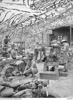 PORT MORESBY, PAPUA. 1942-08. MEN OF AN AUSTRALIAN ORDNANCE WORKSHOP OVERHAULING MOTOR VEHICLES UNDER A CAMOUFLAGE NET