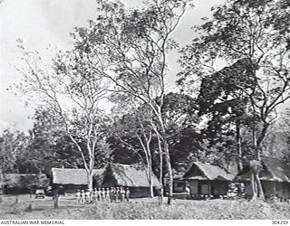 GOODENOUGH ISLAND, NEW GUINEA. 1944-05. THE PERSONNEL OF THE RAN DEPOT LINE UP IN FRONT OF ITS THATCHED BUILDINGS FOR A GROUP PHOTOGRAPH. (NAVAL HISTORICAL COLLECTION)