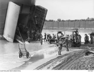 FINSCHHAFEN, NEW GUINEA. 1943-09-22. WHILE TROOPS OF THE FINSCHHAFEN FORCE UNLOAD SUPPLIES FROM AN LST (LANDING SHIP, TANK). A BULLDOZER IS AT WORK SMOOTHING THE BEACH