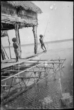 Two men poling an outrigger canoe in front of a house on poles, Papua, ca. 1923 / Sarah Chinnery