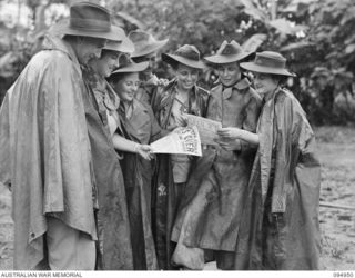 LAE AREA, NEW GUINEA. 1945-08-15. AN EXCITED GROUP OF AUSTRALIAN WOMEN'S ARMY SERVICE AND TROOPS OF FIRST ARMY READING THE FIRST SPECIAL VICTORY PACIFIC EDITION OF "GUINEA GOLD" ANNOUNCING JAPANESE ..