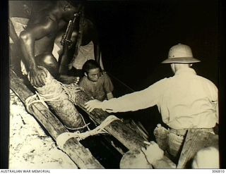 NEW GEORGIA, SOLOMON ISLANDS. 1943-03. A JAPANESE PILOT, CAPTURED BY KENNEDY'S SCOUTS, IS BROUGHT BY CANOE TO THE SEGI COASTWATCHERS STATION (ZGJ5). A US NAVY OFFICER AND CHIEF NGATU, HEAD CHIEF ON ..