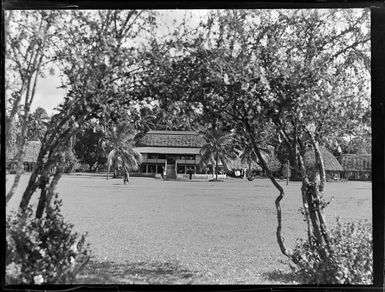 View of a large two story thatched roofed building with fale tele huts surrounding, Apia, Western Samoa