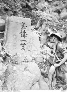 YAULA, NEW GUINEA. 1944-04-10. QX6905 CORPORAL S.H. O'LEARY, 57/60TH INFANTRY BATTALION, EXAMINES AN OBELISK SHOWING A JAPANESE SOLDIER WITH PICK DIGGING AT THE ROCK FACE. THE MONUMENT WAS RAISED ..