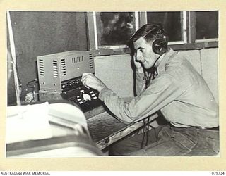 BOSLEY FIELD, BOUGAINVILLE, SOLOMON ISLANDS. 1945-03-15. Q978 SIGNALMAN A.H. WILLIAMS OPERATING THE CONTROL PANEL, AUSTRALIAN ARMY BROADCASTING STATION. THE STATION PROVIDES NEWS AND VARIETY ..