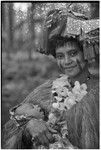 New mother, holding her infant, wears long fiber shawl, flower garland, and skirt valuable on head, paint on face