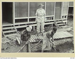 LAE, NEW GUINEA, 1945-05-06. LIEUTENANT-COLONEL M.J. SPENCER, ASSISTANT CONTROLLER OF AUSTRALIAN WOMEN'S ARMY SERVICE, WATCHING NATIVE BOYS WORKING ON DRAINS AT THE AUSTRALIAN WOMEN'S ARMY SERVICE ..