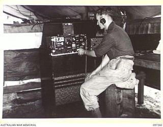 CAPE WOM, NEW GUINEA. 1945-09-29. SIGNALMAN E.J. BULLEN, MONITORING THE NEWS ON NO. 4 RECEPTION SET AS IT IS BROADCAST TO TROOPS FROM RADIO 6 DIVISION, HEADQUARTERS 6 DIVISION. THE STATION REOPENED ..