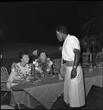 Miss Maglia, on left, with unidentified woman eating a meal and speaking to Fijian waiter, Suva, Fiji, 22 February 1966 / John Mulligan