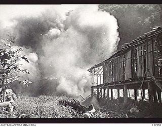 MUBO-SALAMAUA AREA, NEW GUINEA. 1942-08-05. MEMBERS OF 2/5TH AUSTRALIAN INDEPENDENT COMPANY USE AN IMPROVISED BOMB TO SHATTER A NATIVE HUT BELIEVED TO HOUSE JAPANESE TROOPS. IN THE FOREGROUND ..