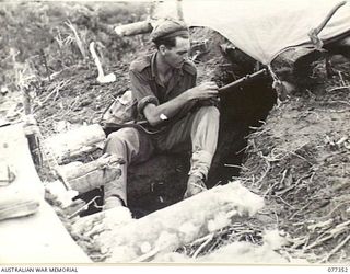 TOROKINA AREA, BOUGAINVILLE ISLAND. 1944-11-30. N264013 PRIVATE L.W. CALLAGHAN, D COMPANY, 9TH INFANTRY BATTALION, CLEANING HIS RIFLE OUTSIDE HIS DUGOUT ON LITTLE GEORGE HILL, A FEATURE CAPTURED ..