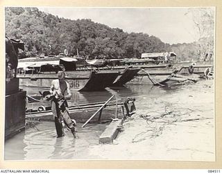 LABU, NEW GUINEA. 1944-12-18. A MEMBER OF 55 CRAFT COMPANY AT THEIR BARGE ANCHORAGE. THE BARGES SHOWN INCLUDE AUSTRALIAN LANDING CRAFT, 5, 15, AND 20S. THIS ANCHORAGE IS A BACKWATER OF THE MARKHAM ..