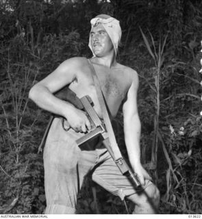 1942-11-23. NEW GUINEA. OIVI. VX38847 LIEUTENANT JOHN R. GREENWOOD, 2/14TH BATTALION CARRIES A THOMPSON SUB MACHINE GUN (TOMMY GUN)  AND WEARS A HANDKERCHIEF AS A SWEAT RAG