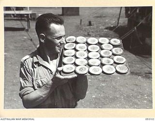 WEWAK AREA, NEW GUINEA, 1945-06-13. PTE N.C. DIXON, HQ 19 INFANTRY BRIGADE, PROUDLY DISPLAYING A TRAY OF JAM TARTS WHICH HE HAS BAKED AND JUST REMOVED FROM THE FIELD OVEN, DURING A COURSE CONDUCTED ..
