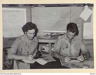 LAE, NEW GUINEA. 1945-05-15. PRIVATE E.M. WALKER (1), TAKING DICTATION FROM CAPTAIN T.M. SHANNON (2), INTELLIGENCE, HEADQUARTERS FIRST ARMY. A FEW DAYS AFTER THEIR ARRIVAL FROM AUSTRALIA AUSTRALIAN ..